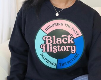 May include: Black crewneck sweatshirt with a circular graphic. The graphic features the words "Black History" in pink, surrounded by the phrases "Honoring the Past," "Inspiring the Future," and "The Future" in a teal and blue color scheme.