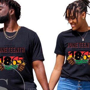 May include: Two people wearing black t-shirts with a graphic design celebrating Juneteenth. The design features the year 1865, a red, yellow, and green flag, and two hands breaking chains.