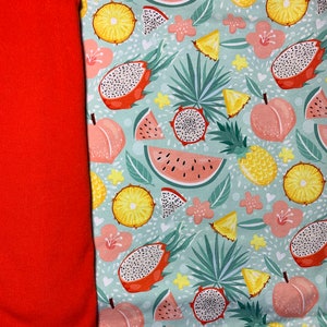 May include: A vibrant fabric featuring a tropical fruit pattern. The design includes dragon fruit, watermelon, pineapple, and peaches on a light blue background. A solid orange fabric is on the left side of the image.