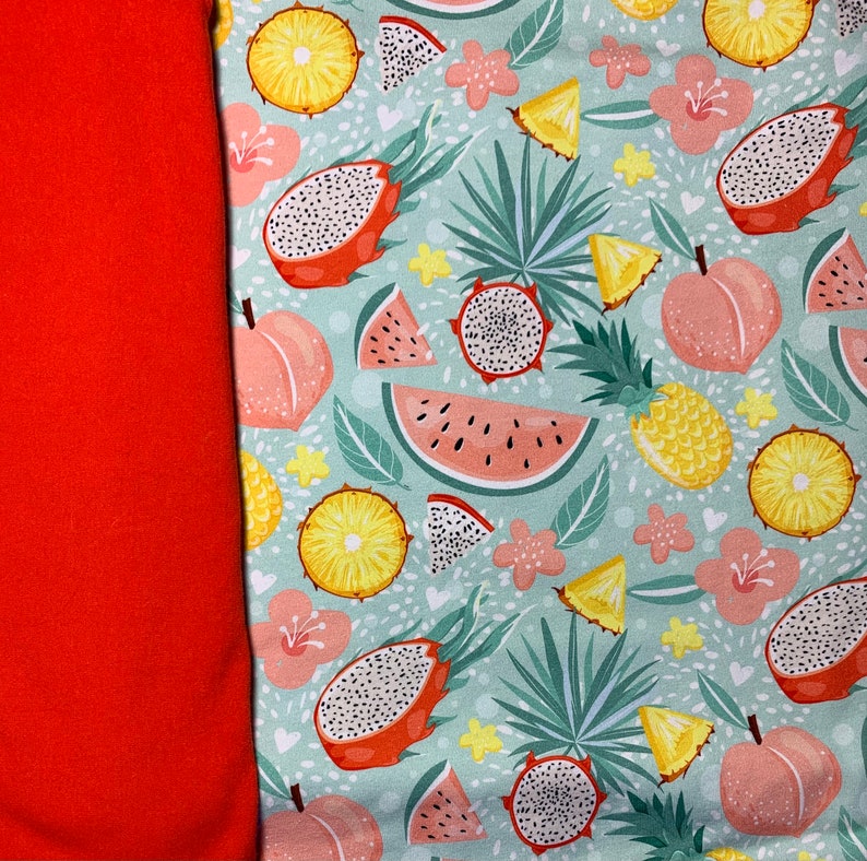 May include: A vibrant fabric featuring a tropical fruit pattern. The design includes dragon fruit, watermelon, pineapple, and peaches on a light blue background. A solid orange fabric is on the left side of the image.