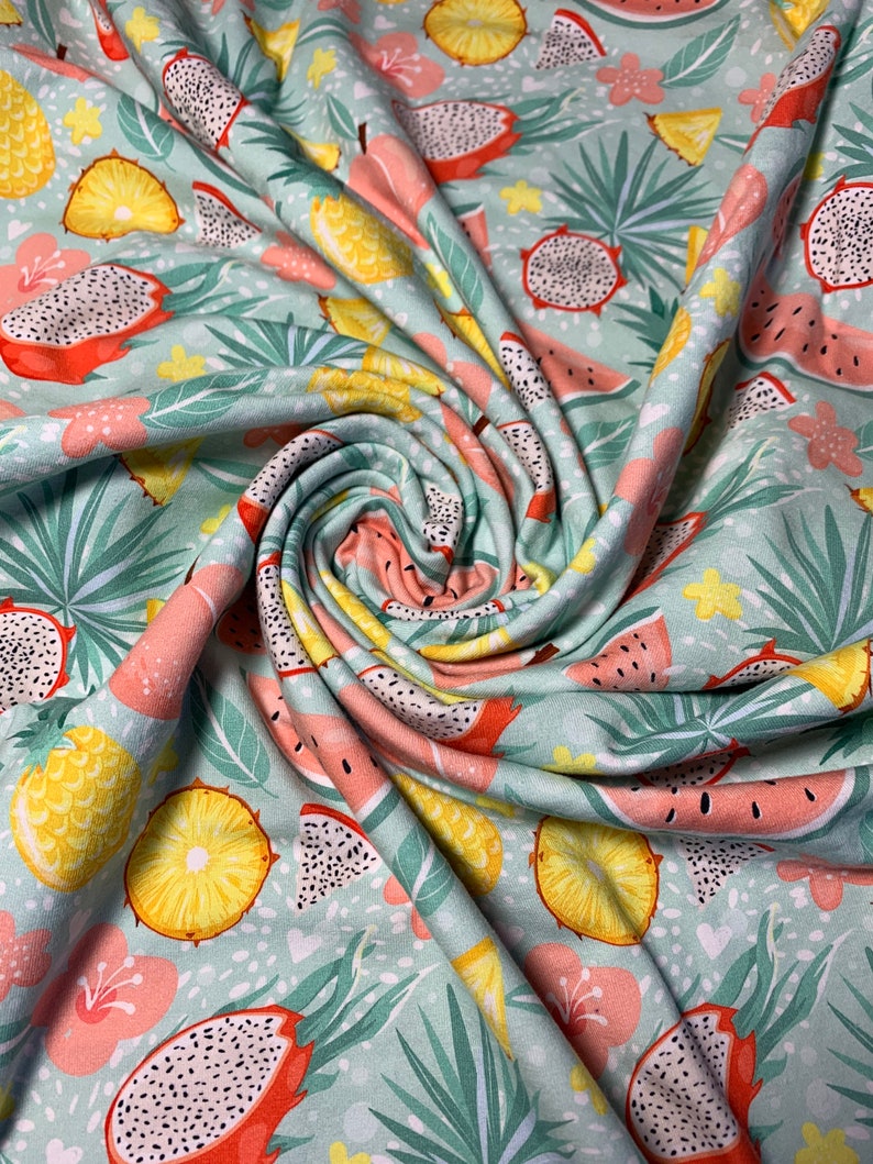 May include: A light teal fabric with a tropical fruit pattern. The design features dragon fruit, pineapples, and watermelon slices, along with pink flowers and green leaves. The fabric is soft and flowing, with a slight sheen.