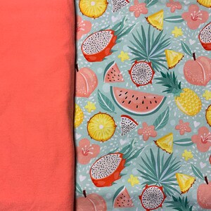 May include: Coral fabric next to a patterned fabric featuring tropical fruits like dragon fruit, watermelon, pineapple, and peaches. The background is a light teal with small white hearts and floral accents.