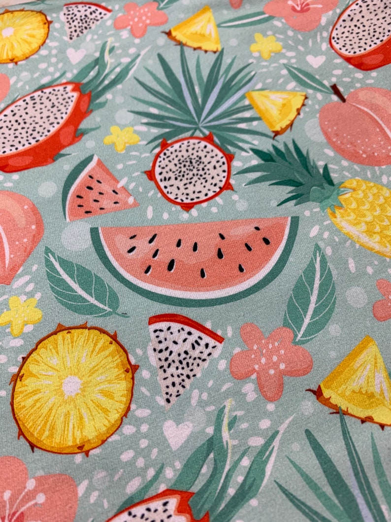 May include: A light teal fabric with a tropical fruit pattern. The design includes watermelon slices, dragon fruit, pineapple, and peach illustrations, along with green leaves and pink flowers. White hearts and dots fill the background.