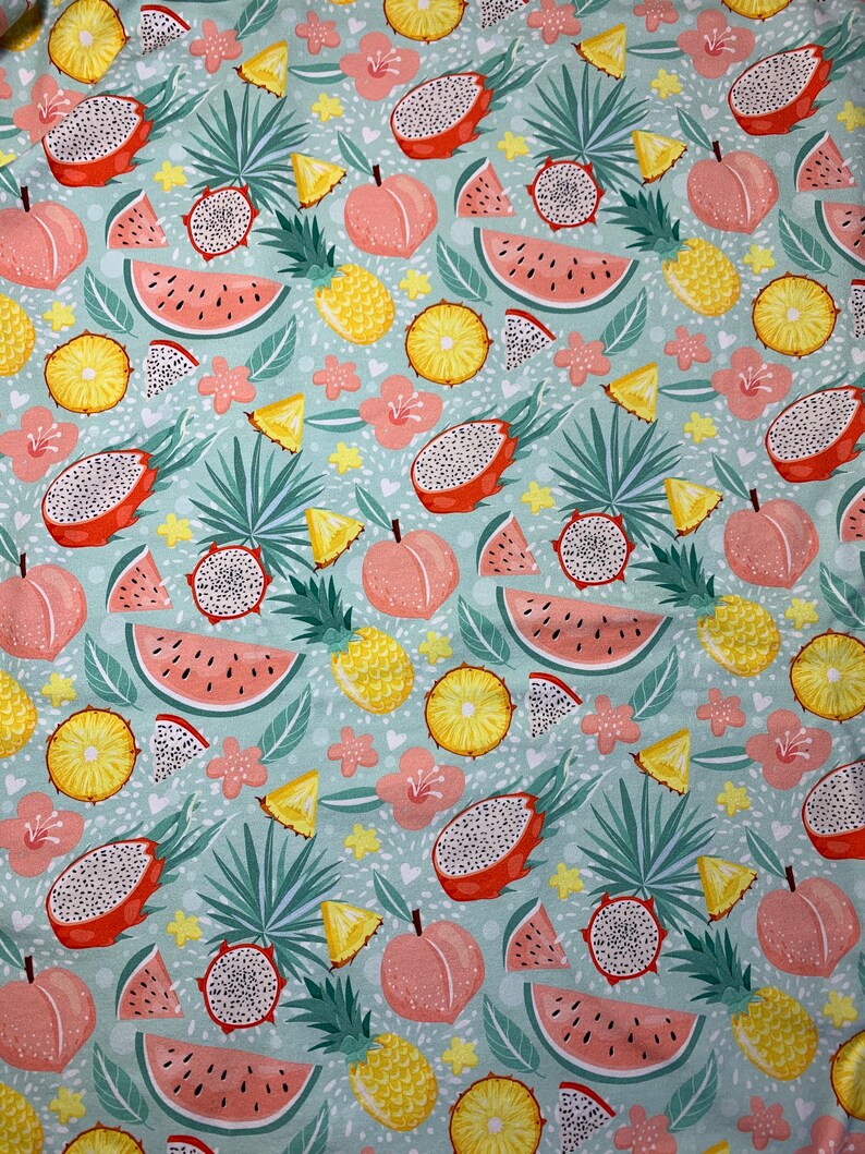 May include: A fabric pattern featuring a repeating design of tropical fruits, including watermelon, dragon fruit, peaches, and pineapples. The fruits are in shades of pink, yellow, and orange, set against a light blue background with green leaves and pink flowers.