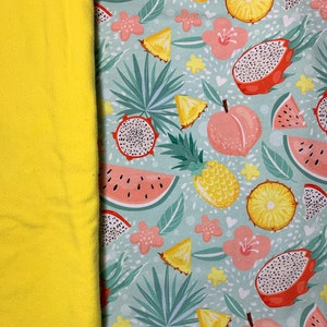 May include: A vibrant textile featuring a tropical fruit pattern. The design includes illustrations of dragon fruit, watermelon, pineapple, and peaches, set against a light blue background with floral accents. A solid yellow fabric is on the left.