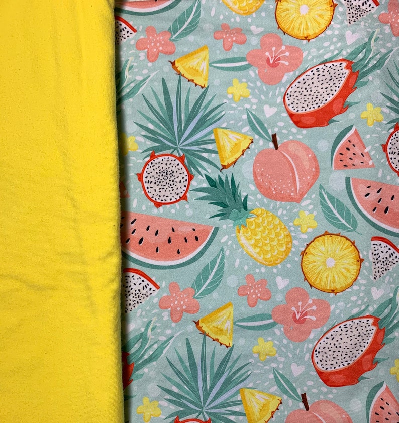 May include: A vibrant textile featuring a tropical fruit pattern. The design includes illustrations of dragon fruit, watermelon, pineapple, and peaches, set against a light blue background with floral accents. A solid yellow fabric is on the left.
