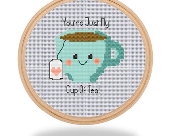 May include: A cross-stitch embroidery hoop with a light blue teacup with a brown lid and a pink heart on the tea bag. The text reads "You're Just My Cup Of Tea!"