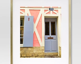 May include: A photograph of a building with a pink wall, white trim, and a blue door. The door has a small window and a brass letterbox. The number "30" is visible above the door.