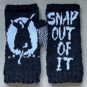 May include: Black knitted fingerless gloves with white text that reads "SNAP OUT OF IT" on one glove and a white graphic on the other. The gloves are made of a textured knit material.