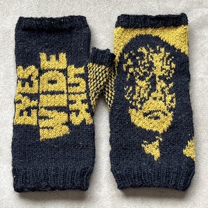 May include: A pair of black fingerless gloves with a yellow knit design. One glove has the words "Rage Against The Machine" knitted into the fabric. The other glove has a yellow knit design of a face.
