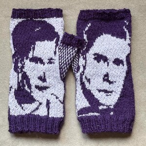 May include: A pair of purple knitted fingerless gloves with white knitted portraits of two people on them.