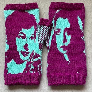 May include: A pair of fingerless gloves knitted in a vibrant magenta and light turquoise color scheme. The design features a stylized portrait of a face integrated into the knit pattern on both gloves, with ribbed cuffs at the top and bottom edges.