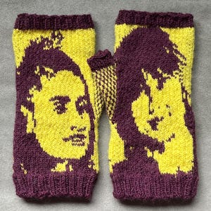 May include: A pair of fingerless gloves knitted with a two-tone color scheme of deep purple and bright yellow. The design features a detailed portrait of a person with voluminous hair on each glove, finished with ribbed cuffs at the top and bottom.