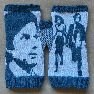 May include: A pair of knitted fingerless gloves. The gloves are primarily light blue with a darker blue design. One glove features a face, and the other depicts two figures. The cuffs and edges are a darker blue.