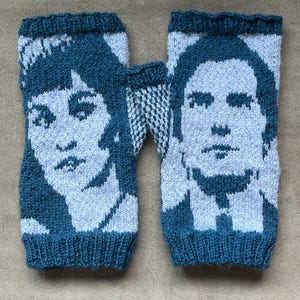 May include: Hand-knitted fingerless gloves in teal and white. Each glove features a portrait design. The gloves are made of a soft, textured yarn. The design is a portrait of a person.