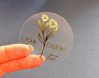Puede incluir: Pegatina redonda transparente con un diseño floral dorado y el texto "YOUR CUSTOM text" impreso en ella.