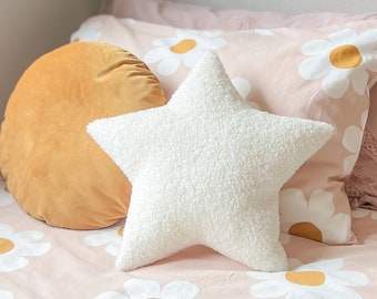 Könnte beinhalten: Ein weißes, flauschiges Kissen in Sternform auf einem rosa Bett mit weißem Gänseblümchenmuster. Ein rundes, senfgelbes Kissen liegt ebenfalls auf dem Bett.