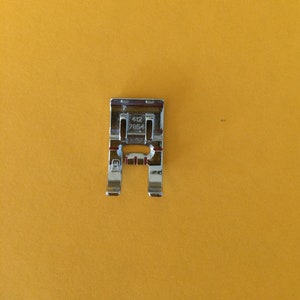 May include: A silver sewing machine foot with the numbers 412 7854 printed on it.