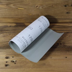 May include: A roll of gray sandpaper with the numbers 1200 and 1000 printed on it. The sandpaper is partially unrolled, revealing a gray sheet. The text "MICRO-MESH" and a phone number are also visible.