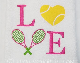 May include: White towel embroidered with the word "LOVE". The "L" and "E" are pink, and the "O" is a yellow tennis ball heart. Two green and pink tennis rackets are crossed below the "L".