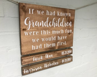 May include: A wooden sign with the text "If we had known Grandchildren were this much fun, we would have had them first."  The sign has two smaller wooden signs attached below it with the names "Hawk Man" and "Harrison Nicholas" and their birth dates.