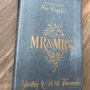 May include: A gray leather-bound journal with gold lettering. The cover reads "866 Devotions for Couples" and "Mr & Mrs Shelby & Will Flowers".