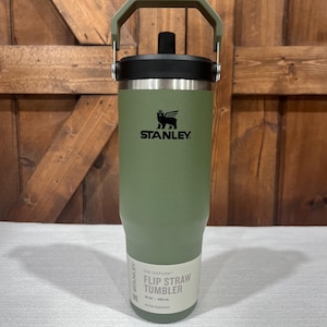 May include: A green Stanley 30 oz / 887 ml stainless steel insulated tumbler with a flip straw lid and a carrying handle. The text "The JEFLOW Flip Straw Tumbler" is printed on the side of the tumbler.
