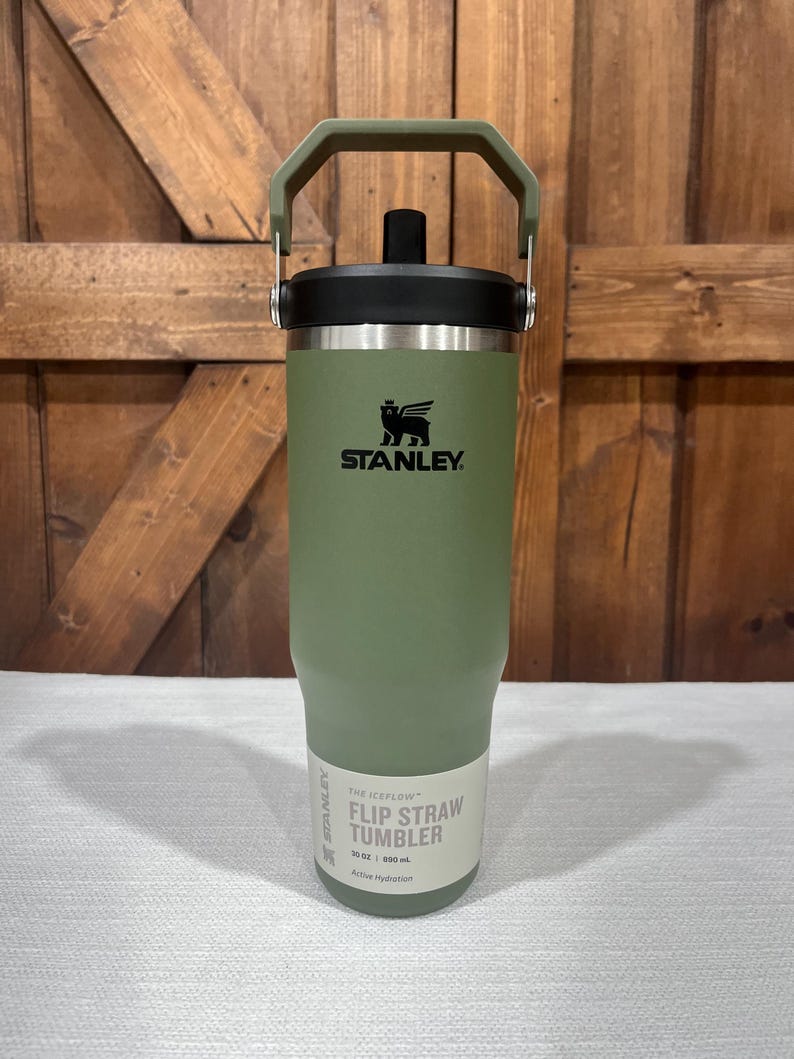 May include: A green Stanley 30 oz / 887 ml stainless steel insulated tumbler with a flip straw lid and a carrying handle. The text "The JEFLOW Flip Straw Tumbler" is printed on the side of the tumbler.