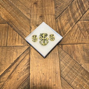 May include: A set of three gold-colored US Navy anchor pins in a white box. The pins feature a stylized anchor with the letters "USN" above it.