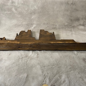 May include: A wooden ship silhouette wall decor, painted in a dark brown colour. The ship is made of multiple layers of wood, creating a dimensional effect.