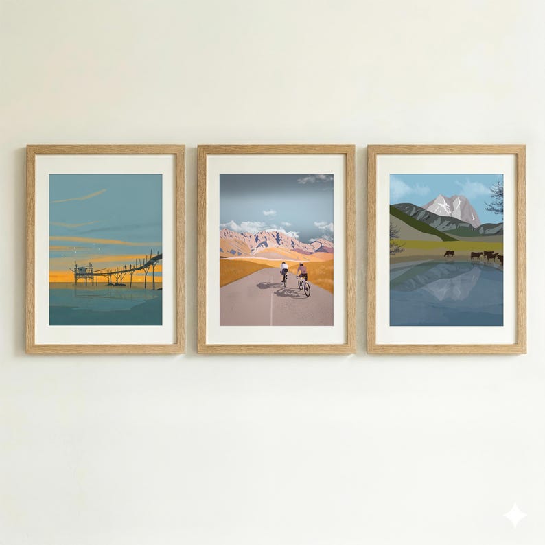 May include: A set of three framed art prints. The left print shows a wooden pier over water at sunset. The center print depicts two cyclists on a road toward mountains. The right print features a lake with cows and a mountain peak in the background.
