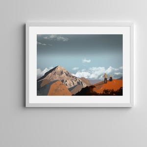 May include: A digital painting of a mountain range with a person standing on a hilltop. The sky is blue with white clouds. The mountains are brown and gray. The person is wearing a brown jacket and blue pants.