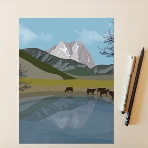 May include: A digital art print depicting a mountain landscape with a lake in the foreground, featuring a group of dark brown cows grazing on the shore. The scene includes a snow-capped peak, rolling hills, and a clear blue sky. Two pens are placed beside the print.
