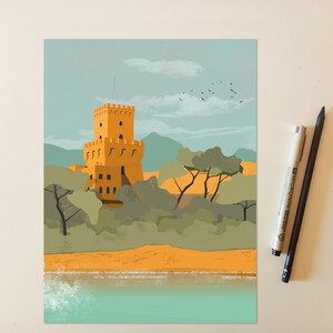 May include: A rectangular art print featuring a yellow stone tower with battlements, surrounded by green trees and mountains under a pale blue sky with birds. The print is positioned next to a white Micron pen and a black pencil on a light surface.