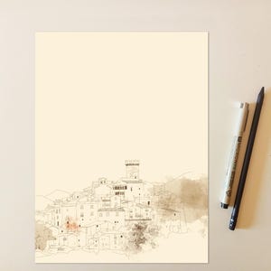 May include: A cream-colored paper print featuring a fine-line ink illustration of a hillside village with a central tower. The drawing includes soft brown watercolor washes. Two pens, one light gray and one black, are positioned to the right side.