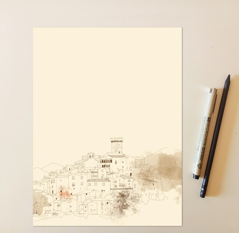 May include: A cream-colored paper print featuring a fine-line ink illustration of a hillside village with a central tower. The drawing includes soft brown watercolor washes. Two pens, one light gray and one black, are positioned to the right side.