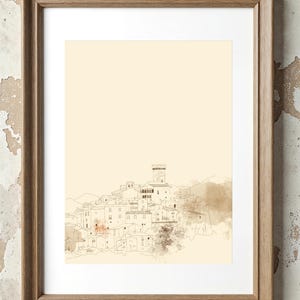 May include: A framed wall art print featuring a fine-line ink drawing of a hillside village with a central tower. The artwork is set against a pale cream background with soft, muted brown watercolor-style washes and is encased in a light wood frame.