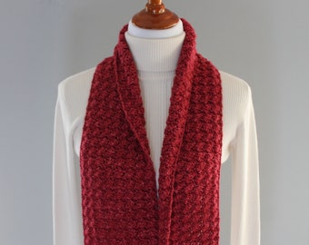 May include: A deep red scarf with a textured, woven pattern. The scarf is draped over a white turtleneck on a mannequin. The scarf's color is a rich, warm tone, and the weave adds visual interest. The scarf is a winter accessory.