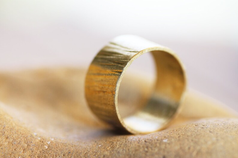 May include: A gold-colored ring with a textured surface. The ring is lying on a brown, textured surface.