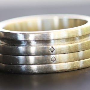 May include: A silver and gold ring with four bands. The top band has a diamond symbol engraved on it, and the band below has a spade symbol engraved on it.