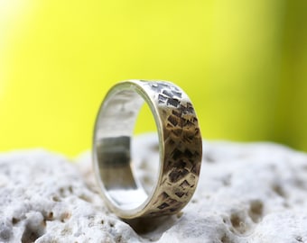 Puede incluir: Un anillo de plata con una banda texturizada. La banda es un diseño de metal martillado con una superficie rugosa y desigual.