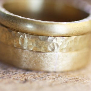 Puede incluir: Primer plano de tres anillos de oro. El anillo superior es liso, mientras que el anillo central tiene una textura martillada. El anillo inferior tiene un acabado mate. Los anillos están apilados, mostrando sus diferentes texturas y acabados.