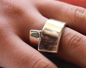 May include: A silver ring with a wide, flat band that is angled and has a smooth, polished finish.