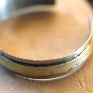 May include: A silver bangle bracelet with a gold band around the edge.