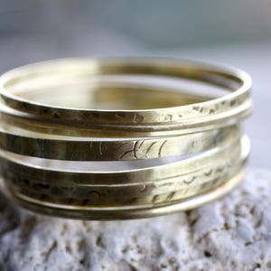 Op de afbeelding: Een stapel van vijf gouden metalen ringen met een gehamerde textuur. De ringen zijn op elkaar gestapeld, waardoor een gelaagd effect ontstaat.
