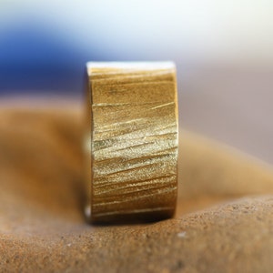 May include: A gold ring with a textured, brushed finish. The ring is wide and has a flat band.