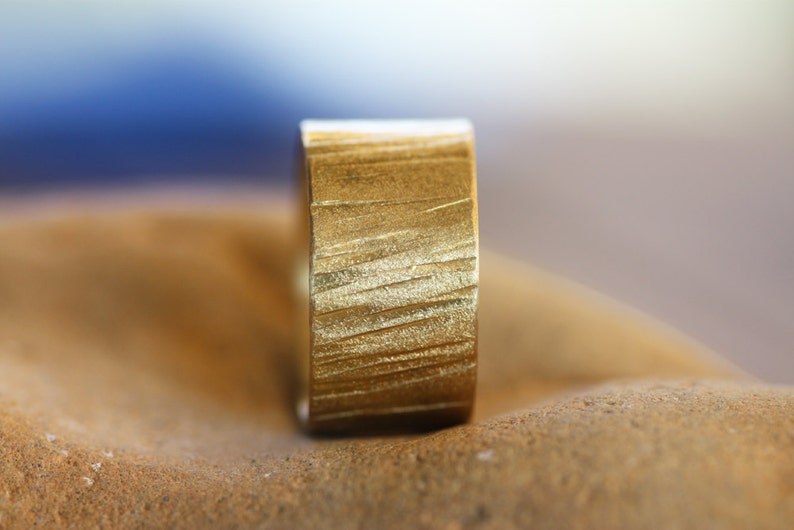 May include: A gold ring with a textured, brushed finish. The ring is wide and has a flat band.