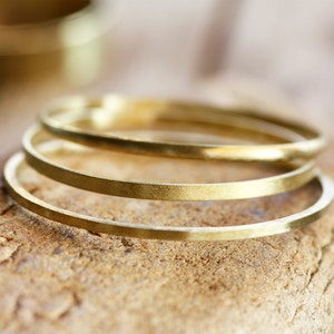 Pode incluir: Três pulseiras de metal douradas empilhadas umas sobre as outras em um pedaço de madeira desgastada.