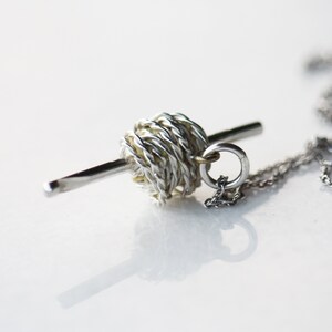 May include: A silver and gold necklace with a yarn ball charm and a needle pendant.