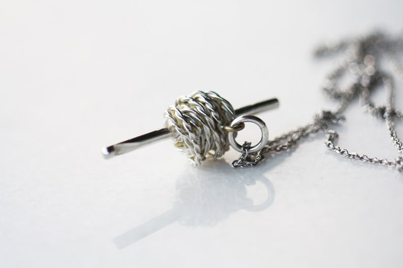 May include: A silver and gold necklace with a yarn ball charm and a needle pendant.